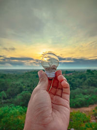 Cropped image of hand holding glass of water against sky