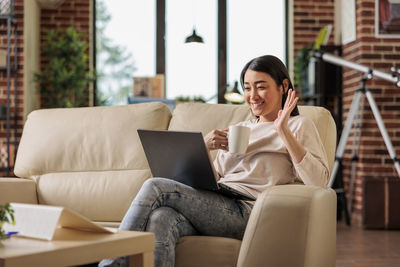Smiling businesswoman holding coffee cup having video call on laptop at home