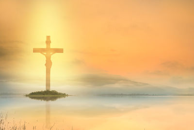 Cross at beach against sky during sunset