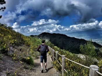 Rear view of man walking on mountain against sky