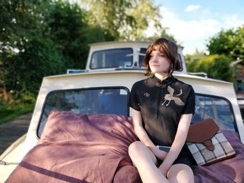 Young woman looking away while sitting on vehicle