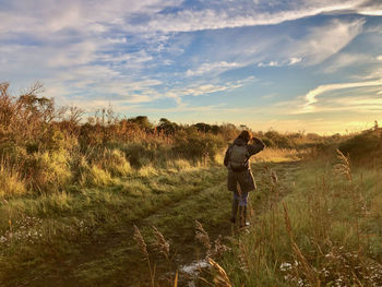 Rear view of a woman walking on a grassy footpath and looking inn the direction of the morning sun