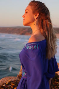 Beautiful woman standing at beach against sky during sunset