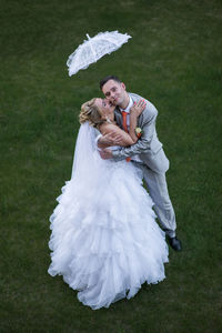 High angle view of bride kissing groom while standing on grassy field
