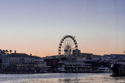Ferris wheel by river against clear sky