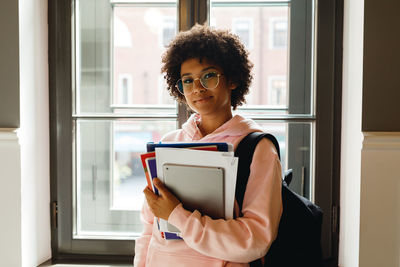 Teenage girl wearing eyeglasses holding books at home