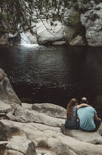 Rear view of friends sitting on rock while looking at lake