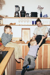 Happy woman playing with son while sitting on kitchen counter at home