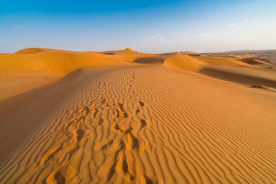 Sand dunes with footprints in them under the blue sky with soft haze on the distant horizon. 