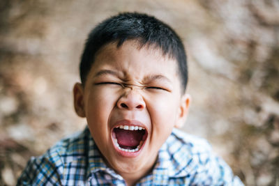 Close-up portrait of cute boy yawning while standing outdoors
