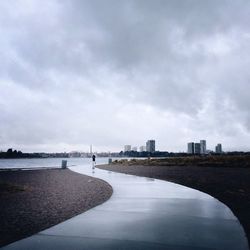 Curved walkway on beach with buildings against sky