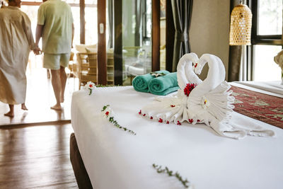 Swan towels on bed with mid adult couple in background at hotel room