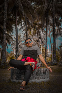 Full length portrait of man sitting on palm tree