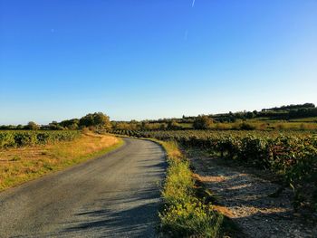 Dirt road amidst field against clear blue sky