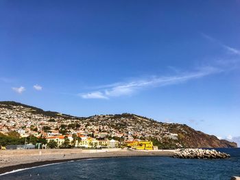 Scenic view of sea by buildings against blue sky