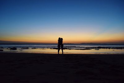 Silhouette people on beach against clear sky during sunset