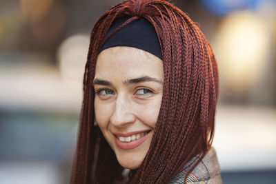 Close-up portrait of smiling woman with braided hair standing outdoors