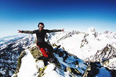 Portrait of male hiker sitting on snowcapped mountain peak against blue sky