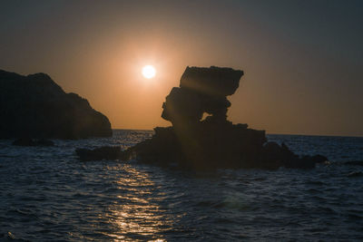 Rock formation in sea against sky during sunset