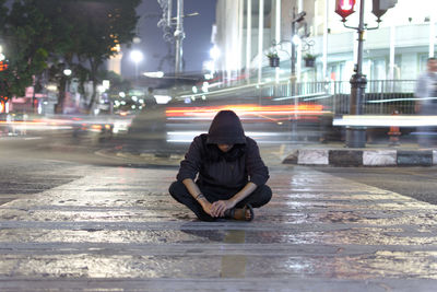 Full length of man sitting on street in city