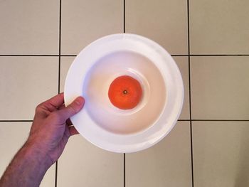 Cropped hand holding orange in plate over tiled floor