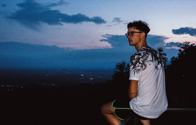 Side view of young man looking away against sky