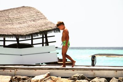 Full length of shirtless boy walking on pier over sea