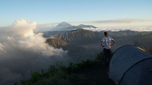 Rear view of man standing on land by tent against sky