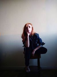 Portrait of beautiful woman sitting against wall