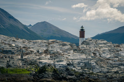 Lighthouse amidst buildings and mountains against sky