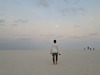 Rear view of man standing at beach against sky at dusk