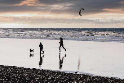 Mother daughter and dog running on the ocean coast at sunset