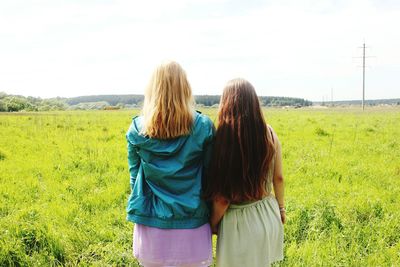 Rear view of women standing on field against sky