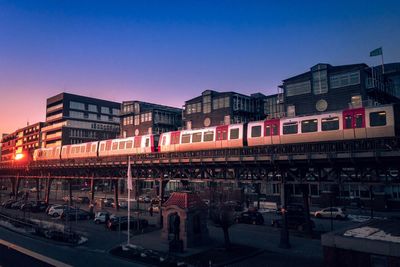 Train on illuminated city against clear blue sky at night