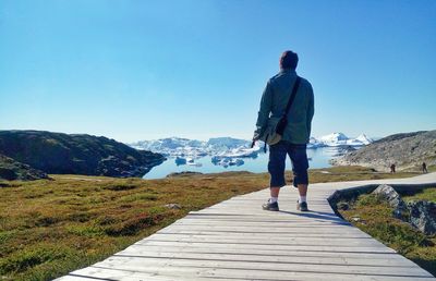 Rear view full length of man standing on boardwalk against icebergs