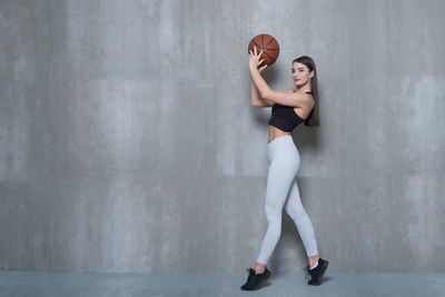 Full length of woman on playing with ball standing by wall