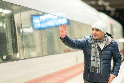 Man waving hand while standing at railroad station platform