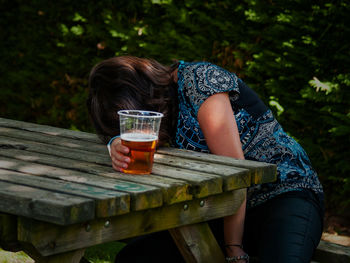 Woman having beer while sitting at table in yard