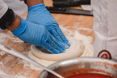 Hands with plastic gloves preparing dough for pizza, focaccia or bread on a wooden board