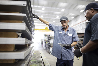 Workers discussing over paper while standing by metal sheets in warehouse