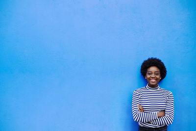 Portrait of smiling young woman standing against blue wall