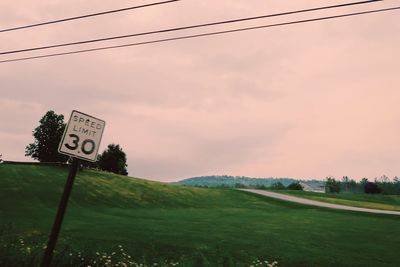 Road sign on field against sky