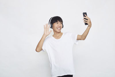 Full length of smiling young man using mobile phone against white background