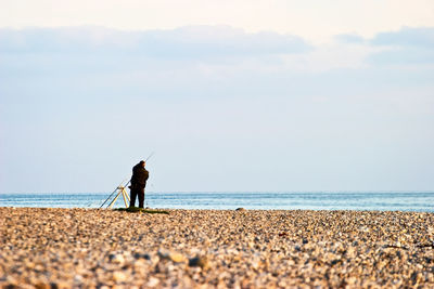 Man fishing on beach against sky
