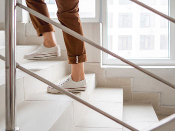 Woman in white sneakers and khaki trousers goes upstairs to her apartment. 