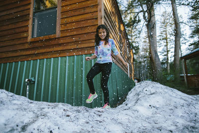 Girl playing in snow at yard against log cabin