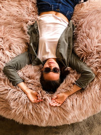 High angle portrait of  a smiling woman lying on fur cushion wearing sunglasses