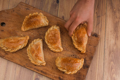 Cropped hand of person grabbing food on cutting board. argentinian empanadas
