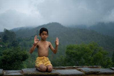 Full length of shirtless man standing on mountain against sky