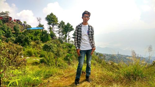 Full length of young man standing by tree against sky